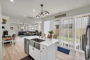 Kitchen with dishwasher, a sink, light wood-style flooring, a center island with sink, and recessed lighting