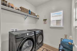 Laundry area with washing machine and dryer, baseboards, and light wood-style floors