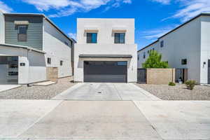 Contemporary house featuring an attached garage, driveway, stucco siding, and a gate