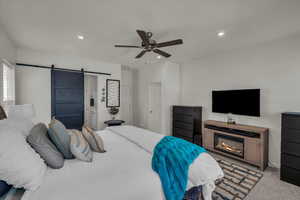 Carpeted bedroom with a barn door, recessed lighting, a ceiling fan, and a glass covered fireplace
