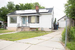 View of front facade featuring a front lawn, an outdoor structure, a chimney, roof with shingles, and solar panels