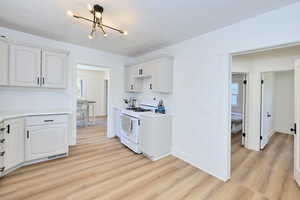 Kitchen featuring white range with gas stovetop, light wood-style floors, a chandelier, light countertops, and white cabinetry