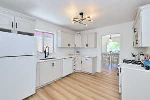 Kitchen featuring white appliances, a sink, a chandelier, light wood finished floors, and white cabinetry