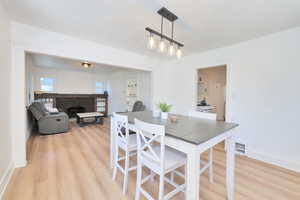 Dining room with light wood-style floors, a brick fireplace, and baseboards