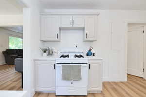 Kitchen featuring white gas range, light LVP flooring, light countertops, and white cabinetry