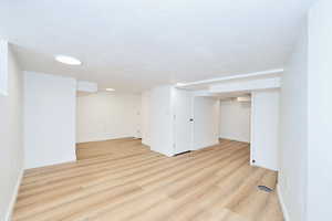 Finished below grade area featuring baseboards, a textured ceiling, and light finished floors