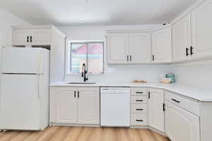 Kitchen featuring white appliances, a sink, a textured ceiling, light wood-style floors, and backsplash