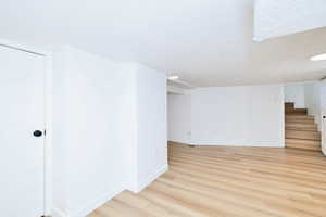 Empty room with light wood-style flooring, baseboards, stairway, and a textured ceiling