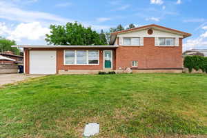 Tri-level home featuring an attached garage, concrete driveway, a front lawn, and brick siding