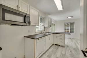 Kitchen featuring stainless steel microwave, dishwasher, a sink, a peninsula, and dark countertops