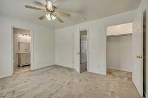 Unfurnished bedroom with a sink, light colored carpet, connected bathroom, and a walk in closet