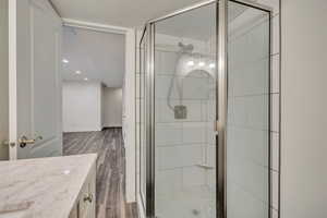 Bathroom featuring wood finished floors, a shower stall, vanity, baseboards, and recessed lighting