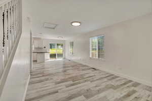 Unfurnished living room with light wood-style floors, baseboards, and attic access