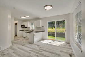 Kitchen featuring dark countertops, white cabinets, light wood finished floors, and baseboards