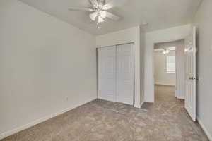 Unfurnished bedroom with light carpet, a closet, baseboards, and a ceiling fan