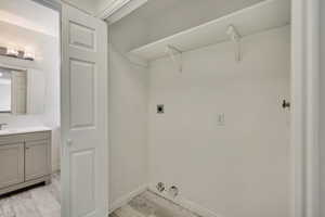 Laundry area featuring electric dryer hookup, light wood-type flooring, and baseboards