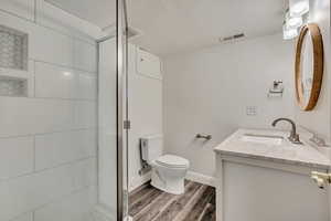 Bathroom with wood finished floors, vanity, toilet, a shower with door, and a textured ceiling