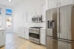 Kitchen with appliances with stainless steel finishes, light countertops, white cabinets, baseboards, and light tile patterned floors