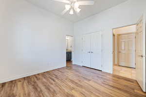 Unfurnished bedroom with light wood-style floors, lofted ceiling, a closet, baseboards, and a ceiling fan