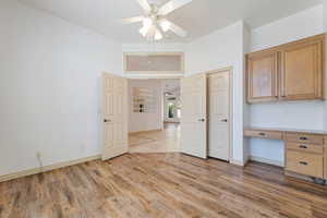 Unfurnished office featuring a ceiling fan, light wood-type flooring, baseboards, built in study area, and a towering ceiling
