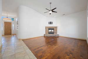 Unfurnished living room featuring lofted ceiling, a ceiling fan, baseboards, light wood finished floors, and a fireplace