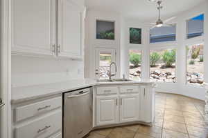 Kitchen featuring stainless steel dishwasher, a sink, ceiling fan, light tile patterned floors, and white cabinets