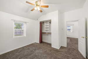 Bedroom 1 featuring dark colored carpet, window, lofted ceiling, baseboards, and a ceiling fan