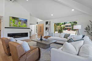 Living room with high vaulted ceiling, light wood-style flooring, a glass covered fireplace, and recessed lighting