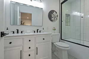 Full bathroom featuring toilet, double vanity, tile patterned floors, and bath / shower combo with glass door