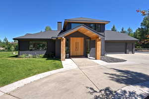Contemporary house featuring concrete driveway, an attached garage, a front lawn, a shingled roof, and a chimney