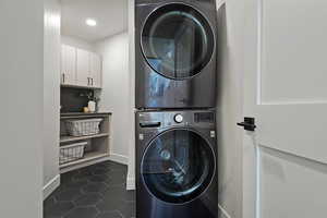 Laundry room with estacked washer and dryer, baseboards, dark tile patterned floors, and recessed lighting