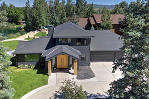 View of front of house with a shingled roof, driveway, a front lawn, a chimney, and a balcony
