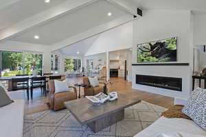 Living area featuring beam ceiling, a glass covered fireplace, light wood-type flooring, high vaulted ceiling, and recessed lighting