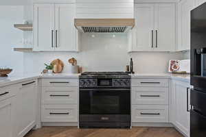 Kitchen featuring stainless steel gas range, open shelves, white cabinetry, light countertops, and tasteful backsplash