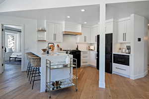 Kitchen with black appliances, custom range hood, a sink, a kitchen breakfast bar, and open shelves