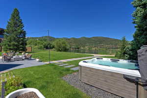 View of grassy yard with a hot tub, a patio area, and a water and mountain view