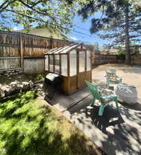 Fenced backyard with a greenhouse, an outbuilding, a grill, and a patio