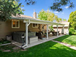 Back of house with a hot tub, a patio area, a chimney, a lawn, and roof with shingles