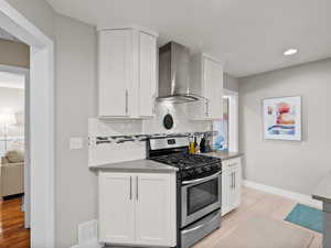 Kitchen with stainless steel gas stove, wall chimney range hood, backsplash, light wood finished floors, and recessed lighting