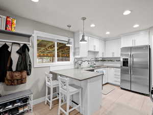 Kitchen with stainless steel refrigerator with ice dispenser, a sink, a peninsula, white cabinets, and decorative light fixtures