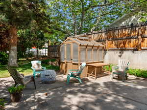 Fenced backyard with a greenhouse, an outdoor structure, and a patio area