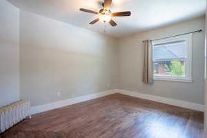 Empty room with radiator heating unit, ceiling fan, baseboards, original wood floors .