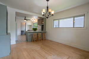 Kitchen featuring baseboards, a peninsula, a chandelier, glass insert cabinets, and a kitchen bar