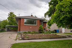 Bungalow-style house featuring brick siding, concrete driveway, a carport, and a chimney