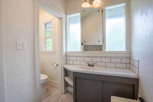 Bathroom featuring toilet, vanity, and backsplash