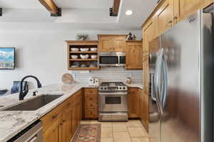 Kitchen featuring appliances with stainless steel finishes, a sink, decorative backsplash, light stone countertops, and light tile patterned flooring
