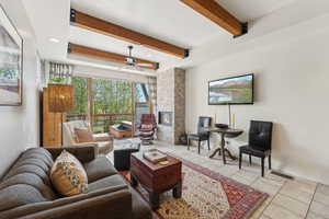 Living area featuring tile patterned flooring, beamed ceiling, a fireplace, ceiling fan, and recessed lighting