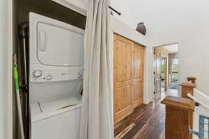 Laundry area with stacked washing machine and dryer, dark wood-style flooring, and baseboards