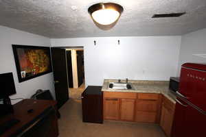 Kitchen with freestanding refrigerator, a sink, stainless steel microwave, brown cabinetry, and a textured ceiling