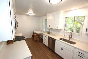 Kitchen featuring dishwasher, a sink, a textured ceiling, light countertops, and white cabinetry